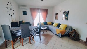 Uma sala de estar moderna com área de jantar, apresentando sofá, cadeiras, mesa e um vaso decorativo.
