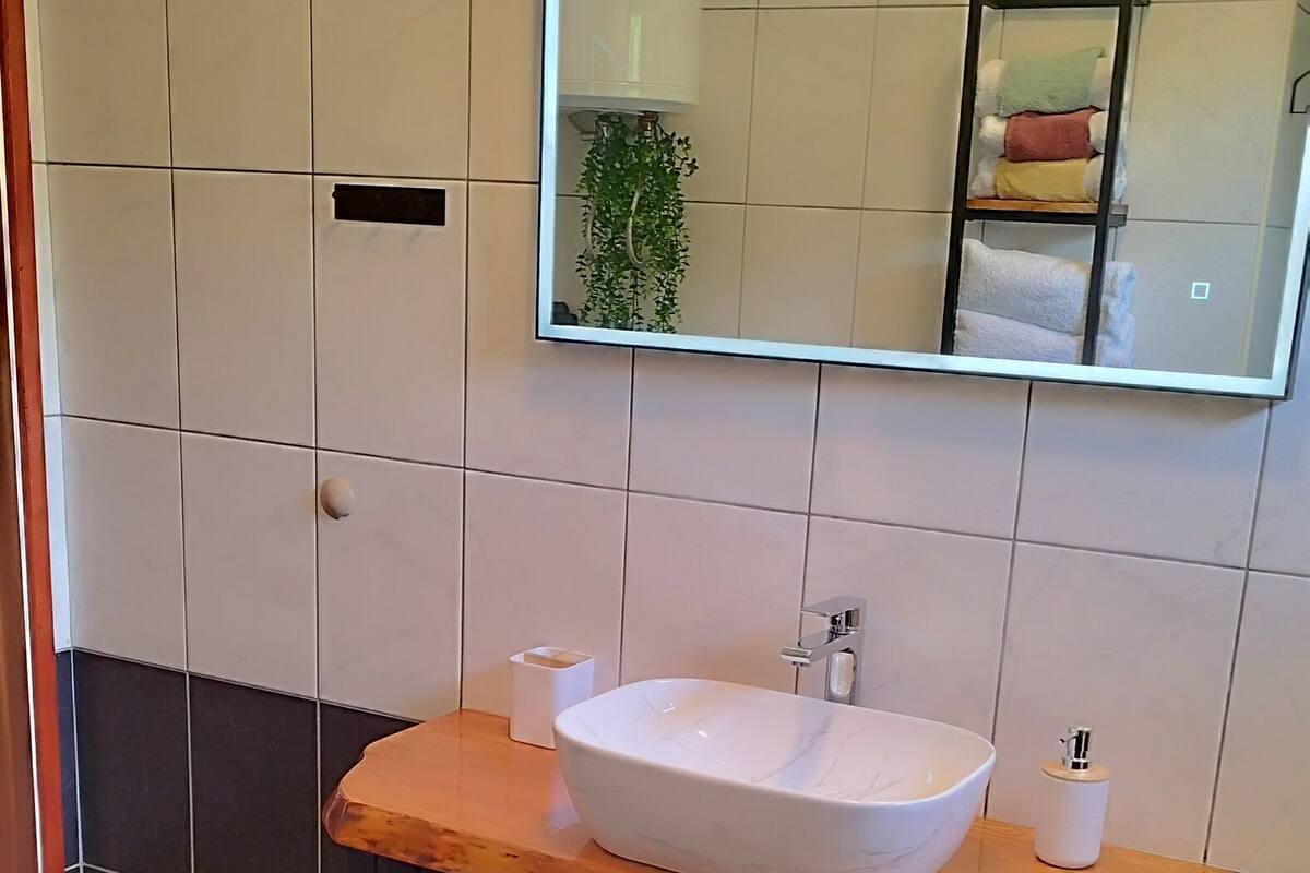A bathroom with a white sink, a mirror above it, a green mat on the floor, and a toilet.