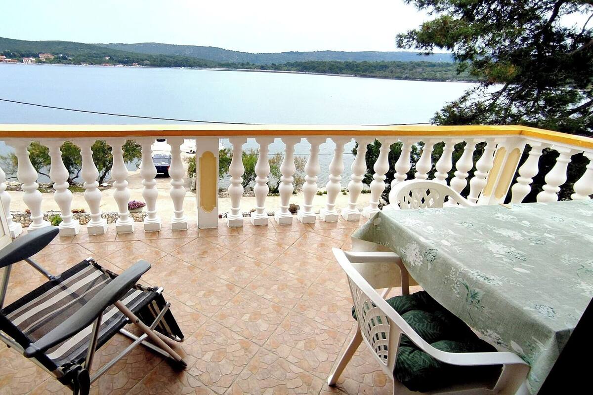 A balcony with a table and chairs, a view of a lake, and a railing with plants.
