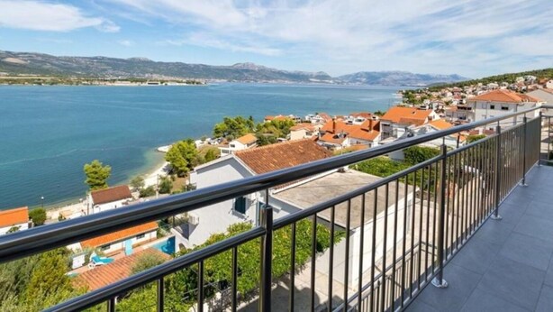 A balcony with a view of a coastal town, a body of water, and distant mountains. - Apartments Petar (Trogir)