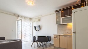 A modern kitchen with a dining area, a sofa, and a TV mounted on the wall. - Apartments Petar (Trogir)