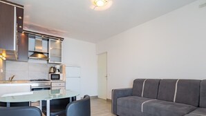 A modern kitchen with a dining area, a sofa, and a door leading to another room. - Apartments Petar (Trogir)