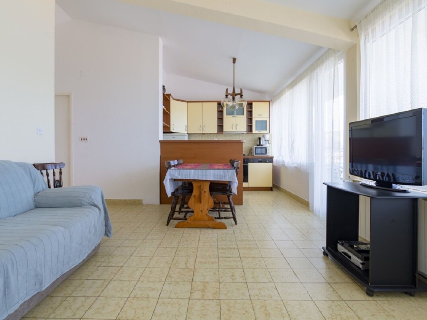 A living room with a sofa, a dining table with chairs, a kitchen area with cabinets and a TV.
