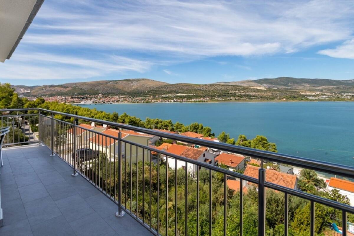Un balcon donnant sur un lac, entouré de verdure et avec une vue sur des collines lointaines.