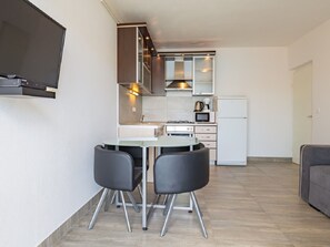 A compact kitchen with modern appliances, a dining area with two chairs, and a flat-screen TV mounted on the wall. - Apartments Petar (Trogir)