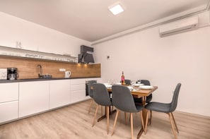 A modern kitchen with a dining area, featuring a wooden countertop, white cabinets, and a dining table set for four. - Apartments Snjeza Family Oasis (Vodice)