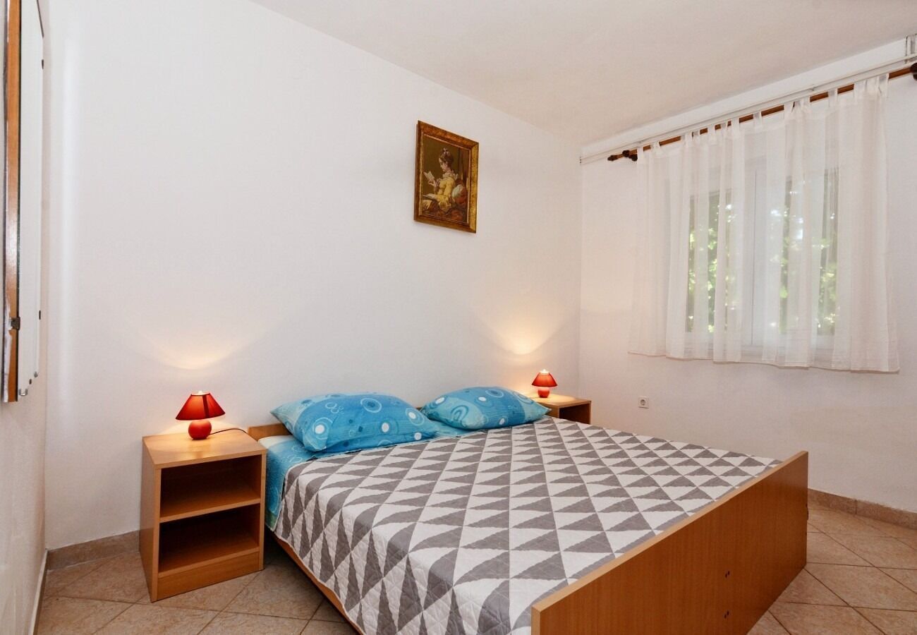 Un dormitorio con una cama, dos mesitas de noche, una lámpara roja en cada una, un cojín azul con estampado y un cuadro en la pared.