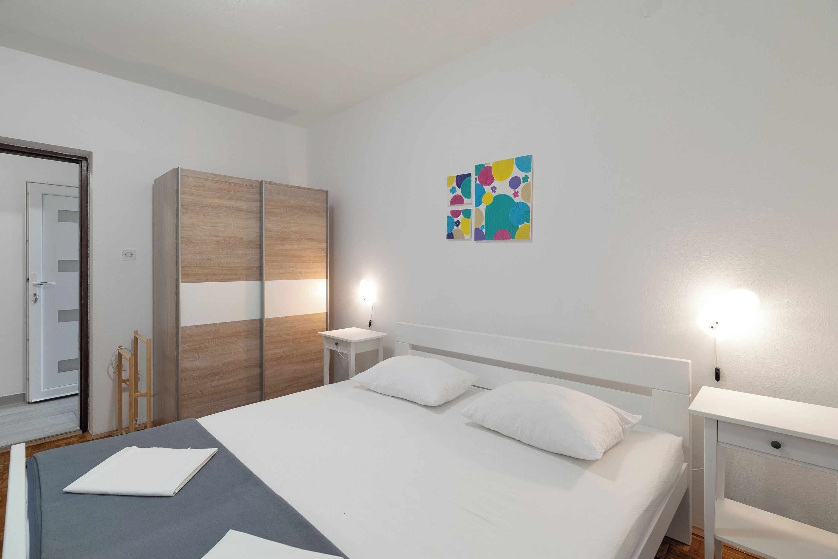 Un dormitorio con cama, mesitas de noche, armario y un cuadro en la pared.