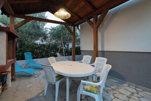 Ένας εξωτερικός χώρος με τραπέζι και λευκές καρέκλες, διακοσμημένος με μια κυκλική πέργκολα από ξύλο.