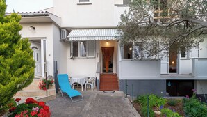 Una propiedad residencial con un patio, una silla azul de salón, una mesa con sillas y una variedad de plantas y flores en macetas.