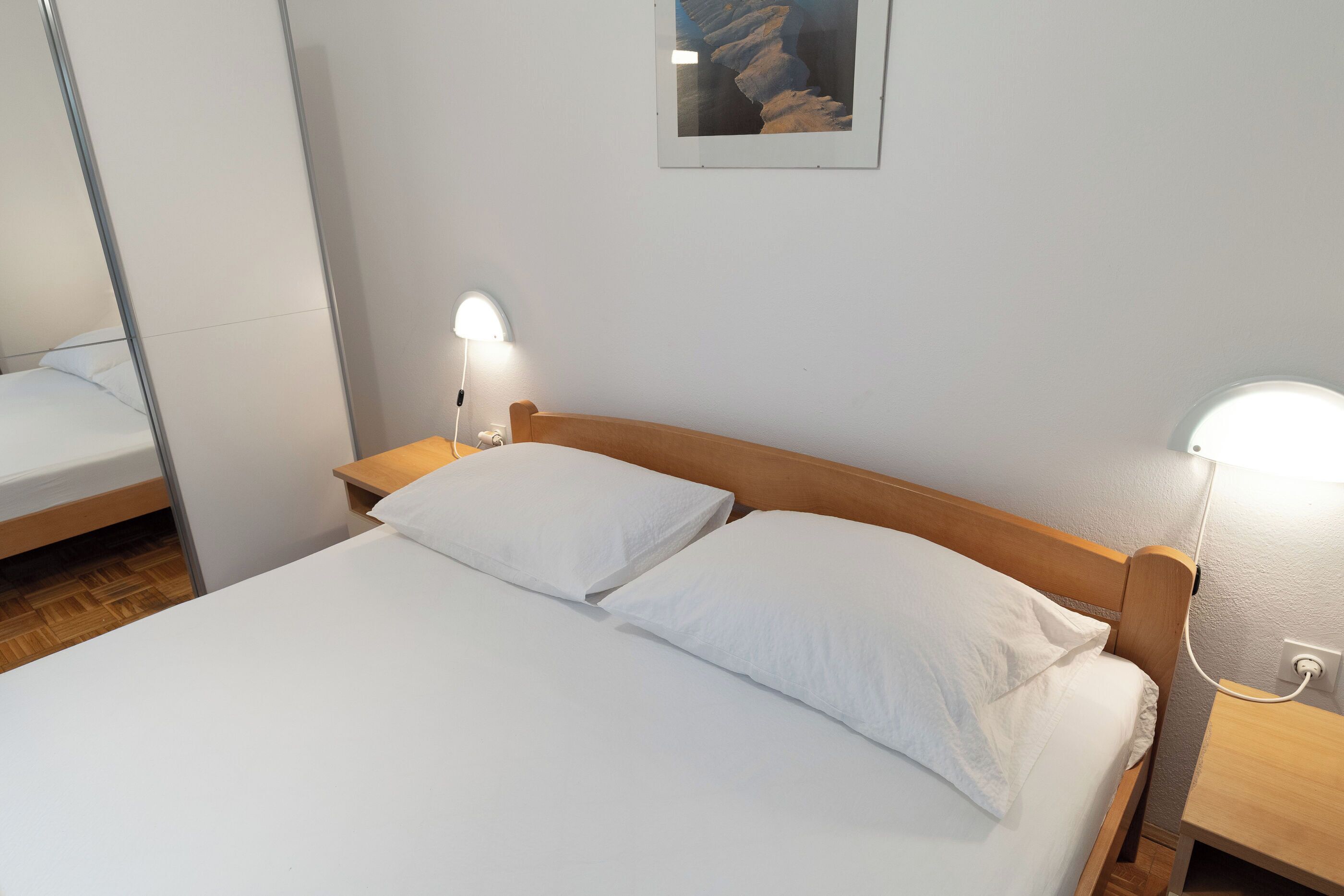 A neatly made bed with white linens and pillows, a wooden headboard, and bedside lamps.