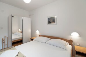 A hotel room with a bed, bedside tables, a mirror, and a painting on the wall. - Apartments Pere (Povljana)