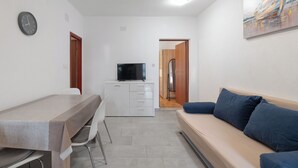 Un espacio habitable compacto con kitchenette, una mesa de comedor, un sofá y una televisión.