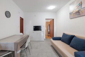 A compact living space with a kitchenette, a dining table, a sofa, and a television. - Apartments Pere (Povljana)