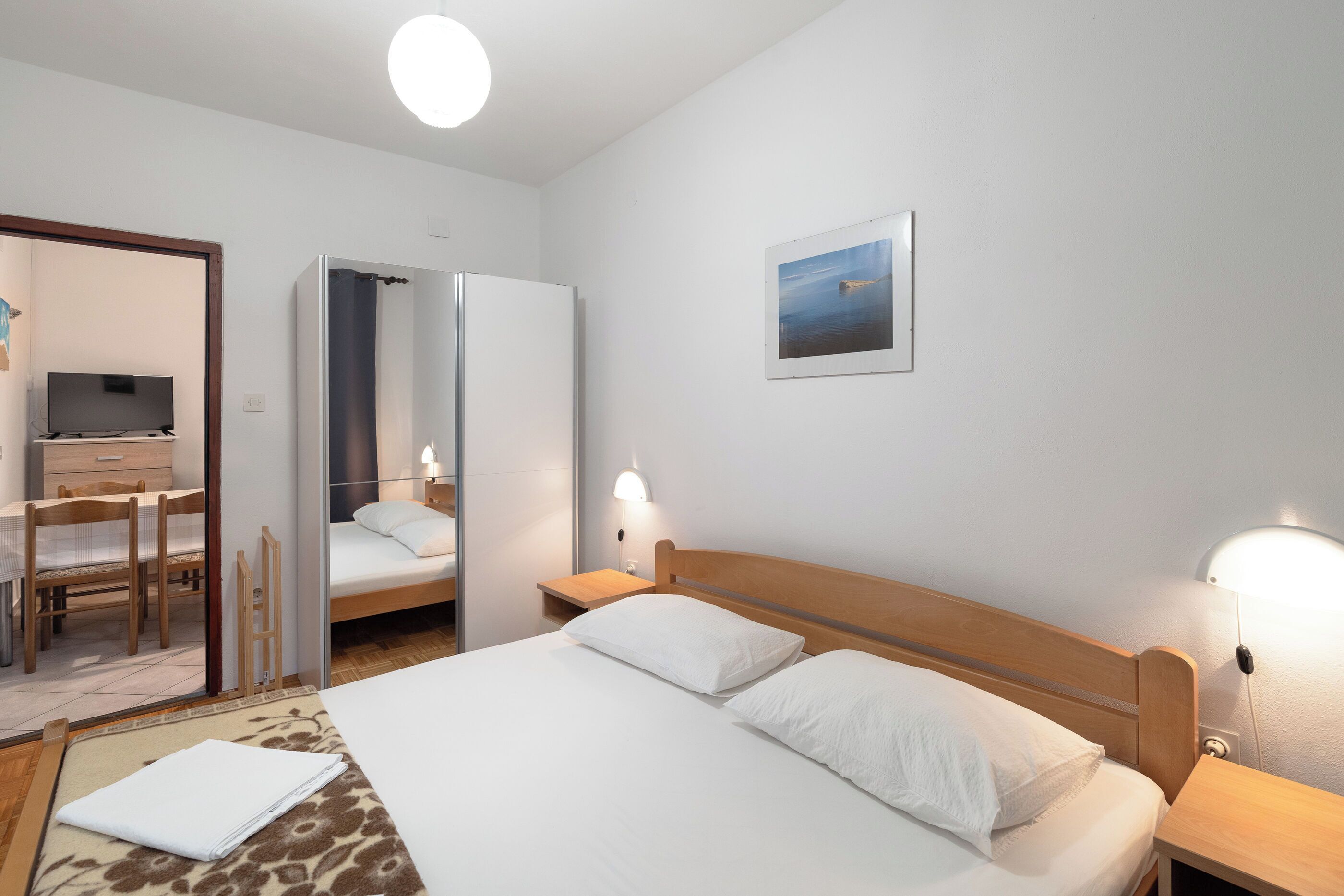 Habitación de hotel con cama, lámparas de noche, escritorio con silla, televisor y un cuadro en la pared.