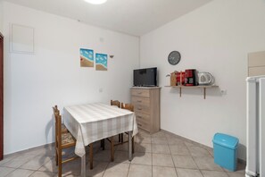 A small, tidy room with a dining table, chairs, a television, a clock, and a trash bin. - Apartments Pere (Povljana)