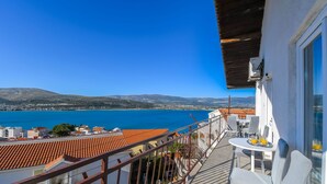 A balcony with a view of the sea and distant hills, a table with chairs, and a small table with a tray of drinks. - Apartment Doktor (Trogir)
