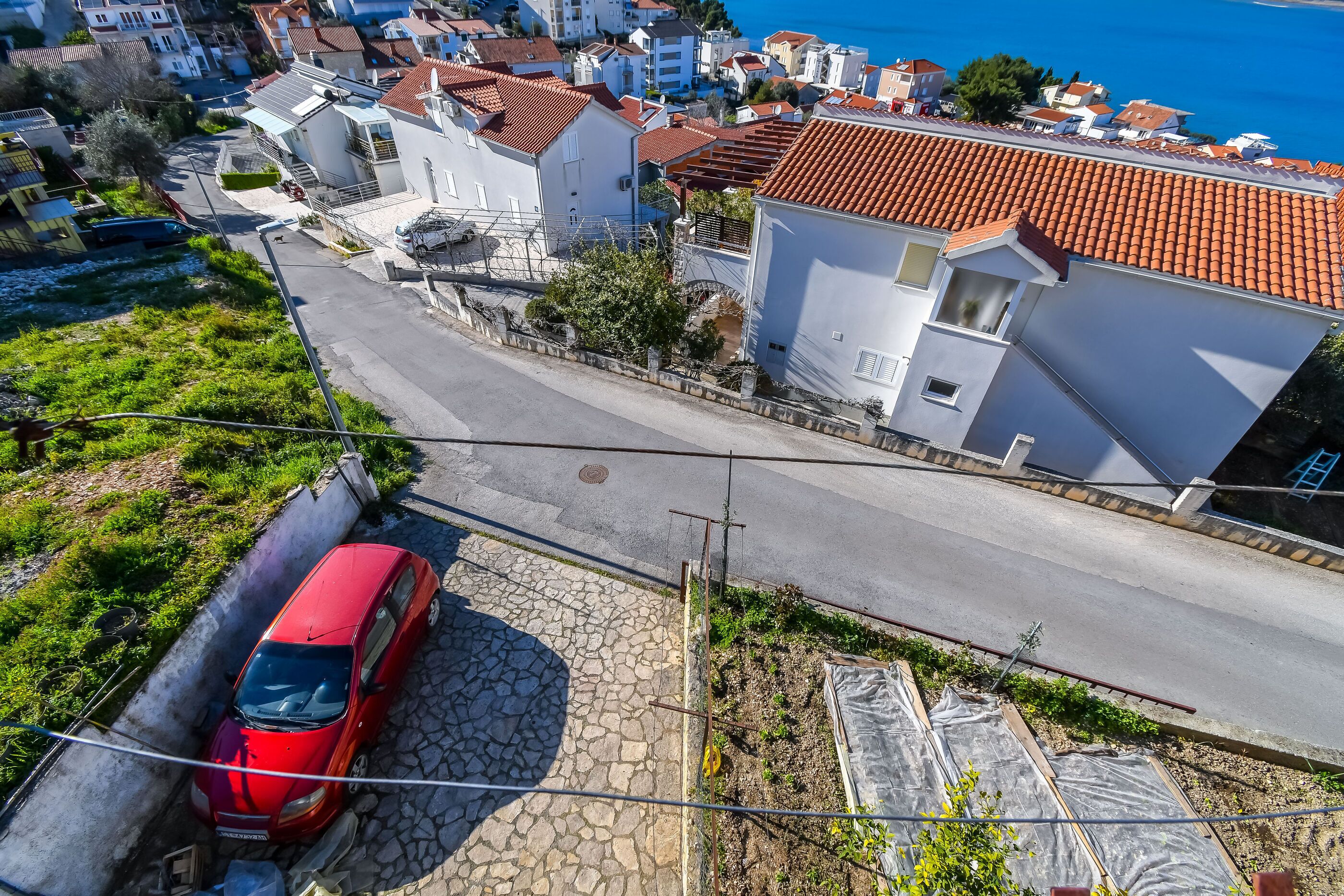 A red car parked on a cobblestone street in a residential area with white buildings and a clear blue sky.
