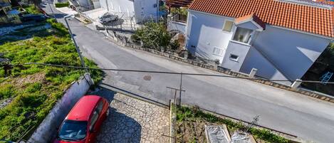 A red car parked on a cobblestone street in a residential area with white buildings and a clear blue sky.