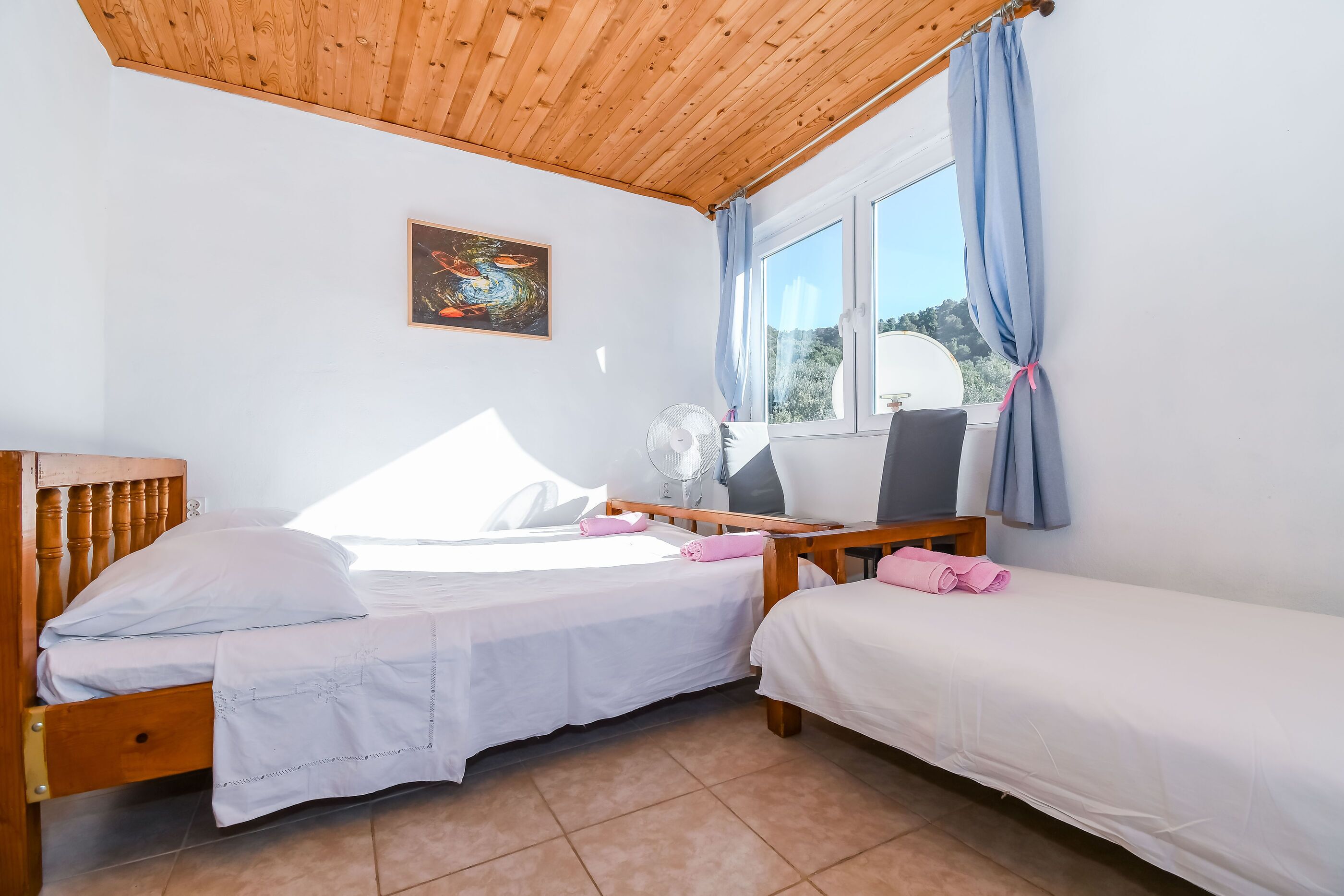 A bedroom with two beds, a ceiling fan, a window with curtains, and a painting on the wall.