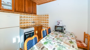 A compact kitchen with wooden cabinets, a refrigerator, an oven, a microwave, and a dining table with chairs. - Apartment Doktor (Trogir)