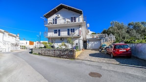 A two-story building with a balcony, a red car parked in front, and a cobblestone street. - Apartment Doktor (Trogir)