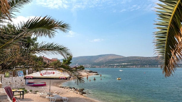 A beach with a clear view of the sea, a few boats, and a building with a sign. - Apartment Doktor (Trogir)