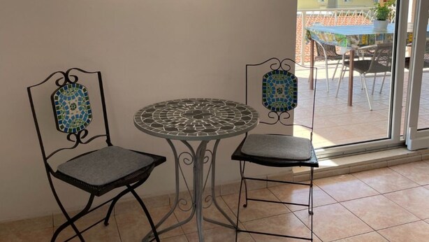 A balcony with two chairs and a table, a tiled floor, and a view of the sea and buildings. - Apartments Ivan (Jelsa)