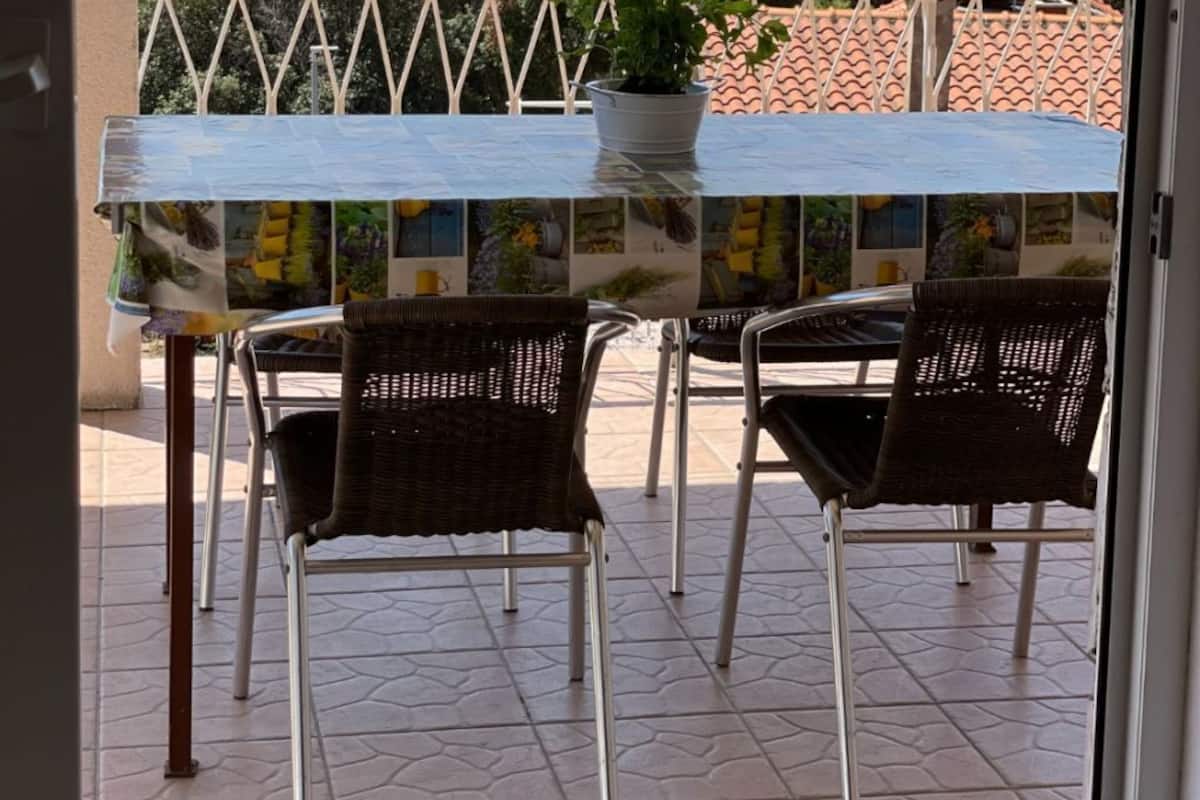 A balcony with a table and chairs, a potted plant, and a view of the sea and mountains.