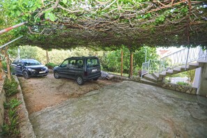 A covered parking area with two cars parked under a canopy of trees. - Apartments Ivan (Jelsa)