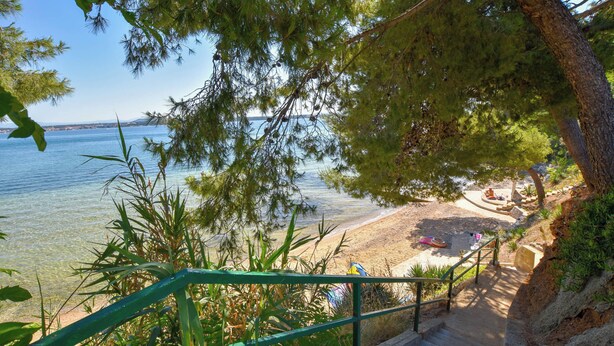 Ein Strand mit klarem Wasser, einer Treppe, die zum Ufer führt, und Blick auf das Meer.