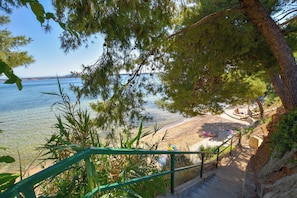 Une plage à l’eau claire, un escalier descendant vers le rivage et une vue sur la mer.