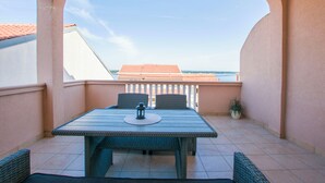 Ein Balkon mit Tisch und Stühlen, einem Blumentopf und Blick auf Gebäude und Himmel.