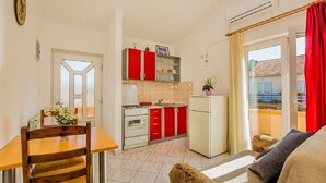 Eine kleine Küche mit roten Schränken, einem weißen Kühlschrank und einem Essbereich mit Holztisch und Stühlen.