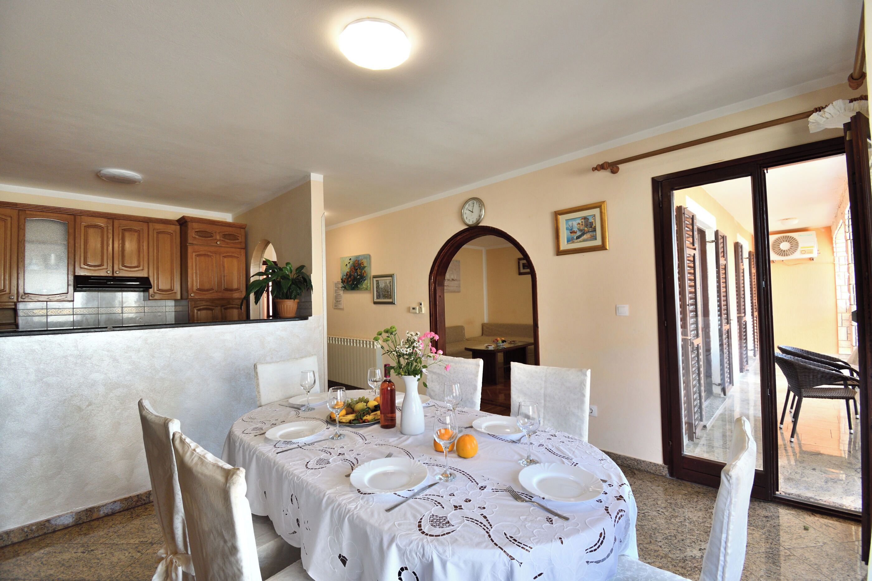 A dining area with a table set for four, a kitchen in the background, and a view of the outside balcony.