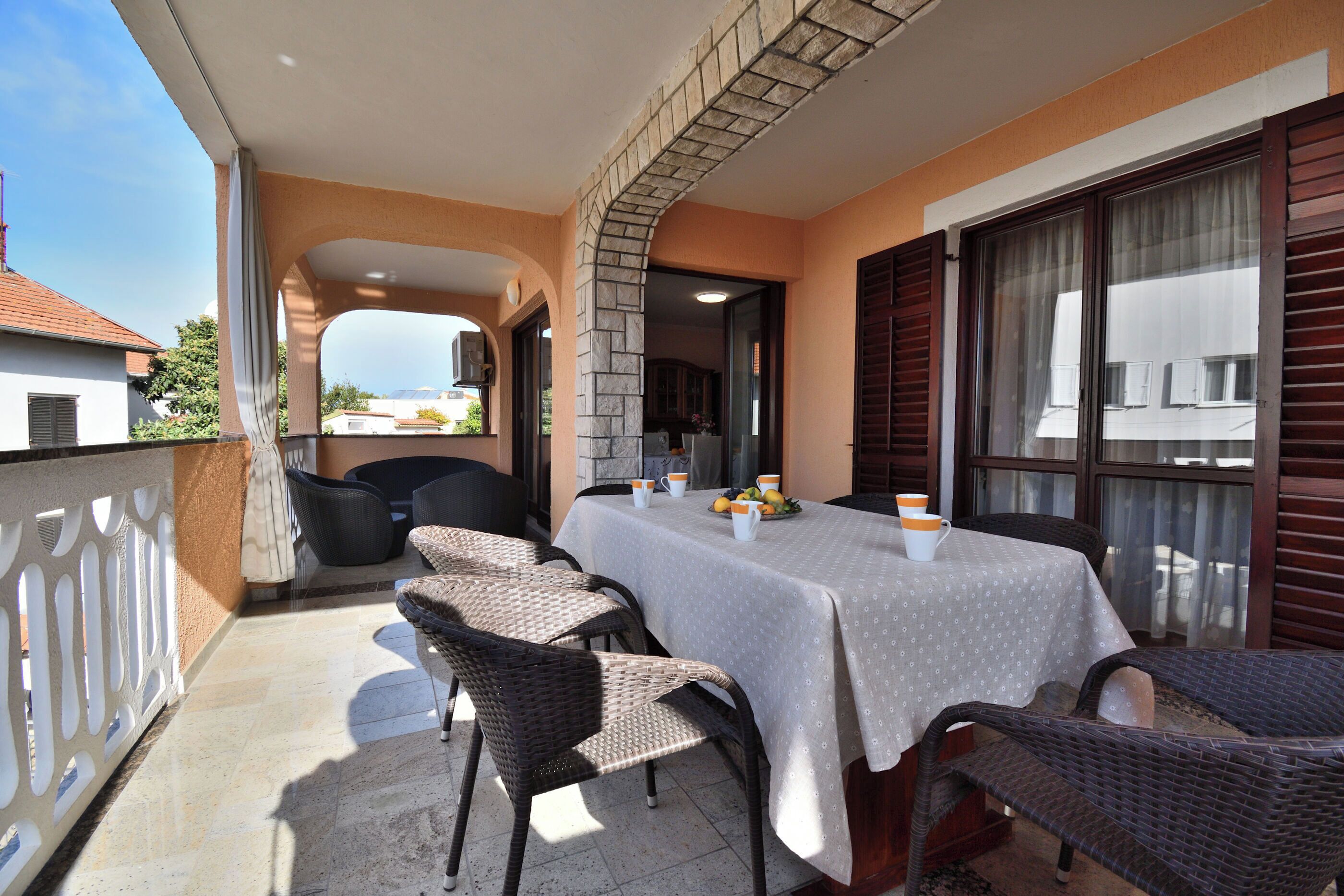A balcony with a table set for two, wicker chairs, and a view of the sea.