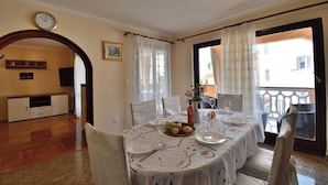 Un comedor con una mesa dispuesta para cuatro, un reloj en la pared y vistas a través de la ventana.