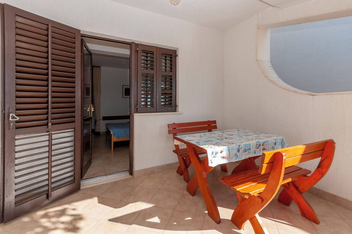 Een kamer met een houten tafel en stoelen, een raam en een deur met luiken.
