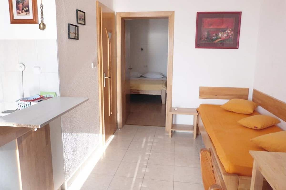 Een compacte kamer met een kitchenette, een bed met oranje beddengoed en een klein nachtkastje.