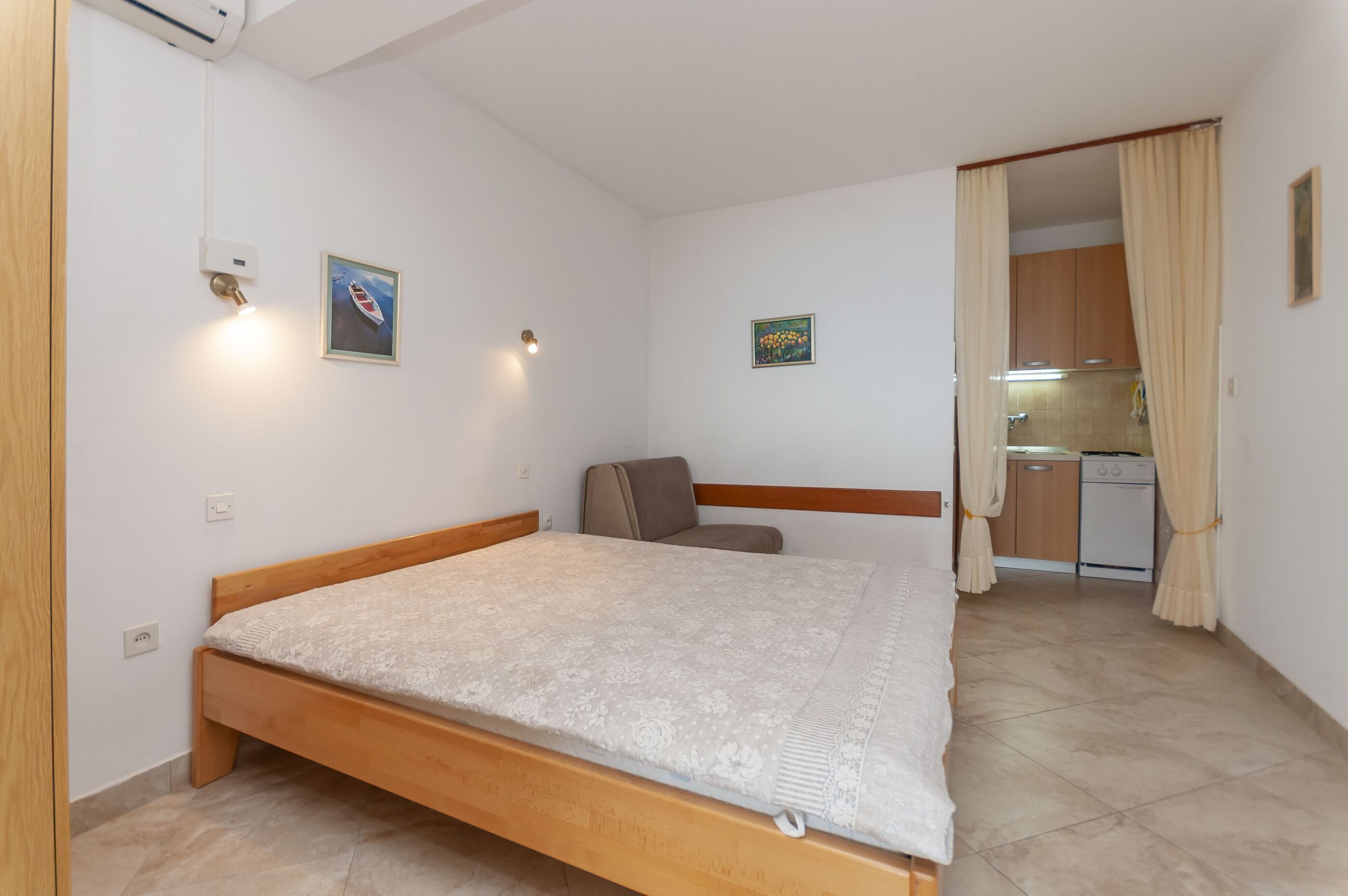 Une chambre à coucher avec un lit en bois, un petit bureau et, au fond, un coin cuisine.