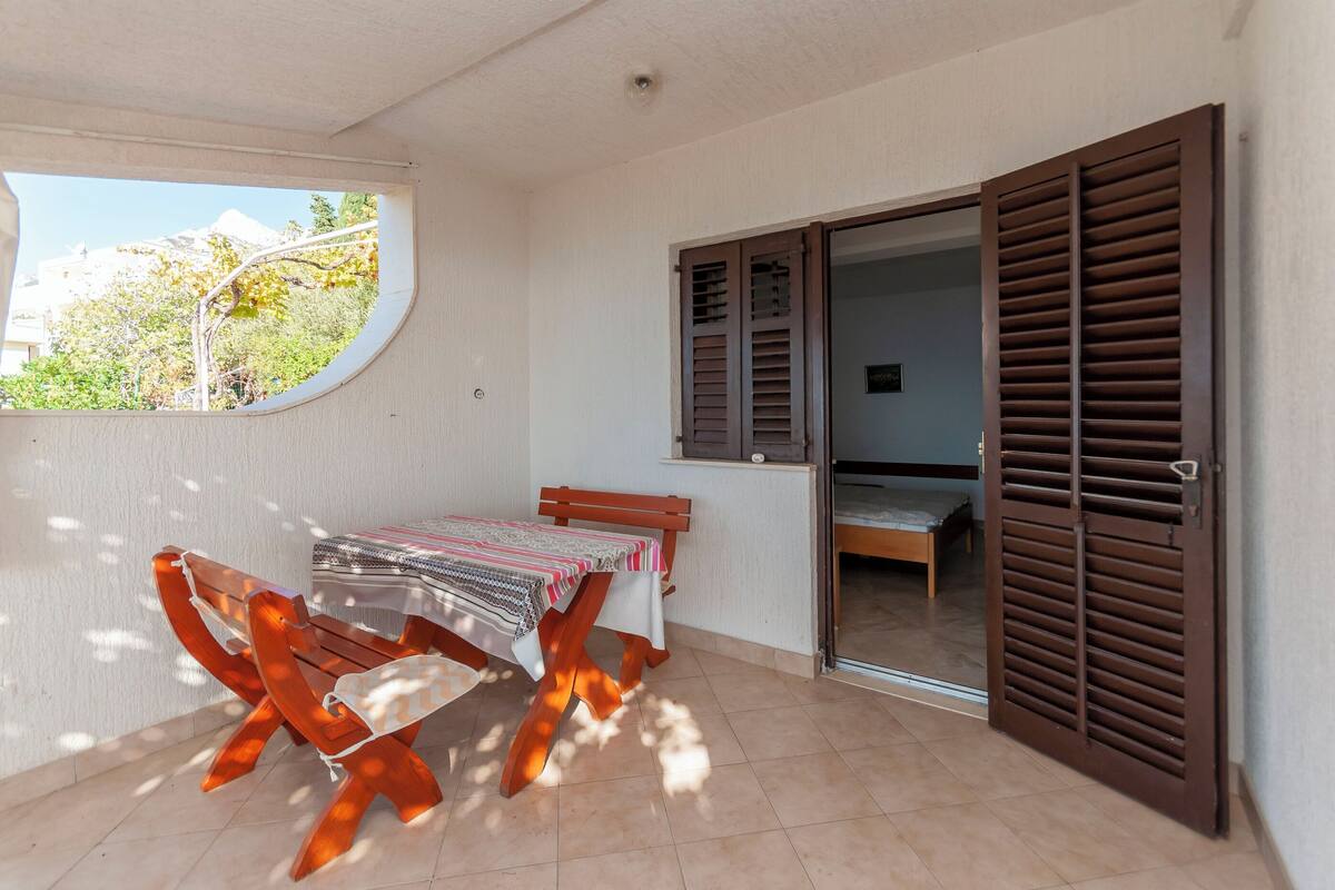 Een balkon met een tafel en stoelen, uitzicht op groen, en een schuifdeur.