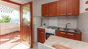 A compact kitchen with wooden cabinets, a gas stove, a refrigerator, and a sink. - Apartments Niko (Omis)