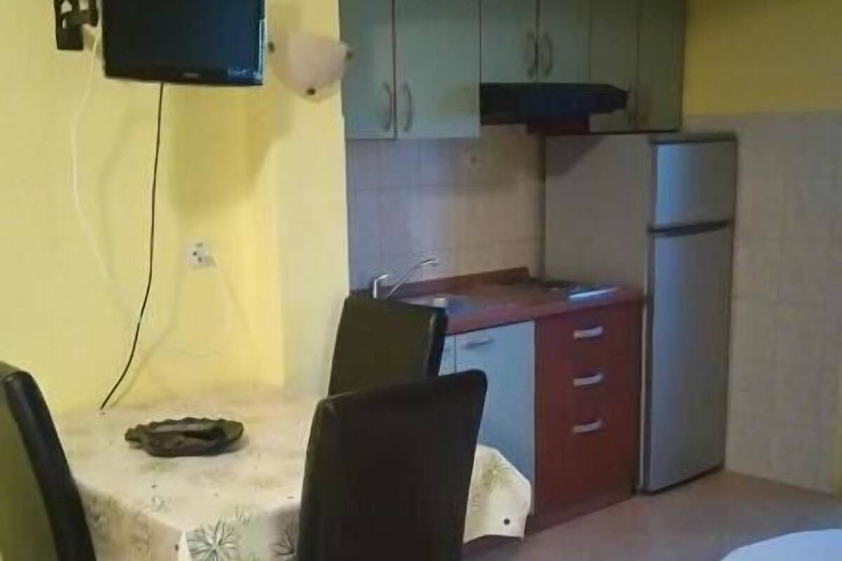 A small kitchen with a dining table and chairs, a TV mounted on the wall, and a bed in the corner.