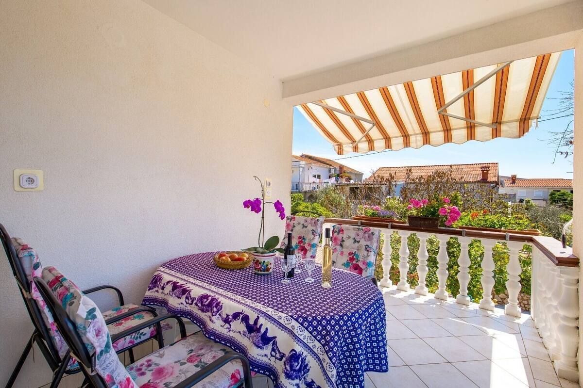 A patio with a table set for two, chairs, and a decorative tablecloth.