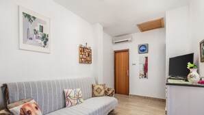 A living room with a sofa, a television, a small table with a vase, and a door leading to another room. - Apartments Masa (Povljana)