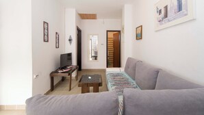 A living room with a grey sofa, a small wooden table, a TV, and framed pictures on the walls. - Apartments Masa (Povljana)