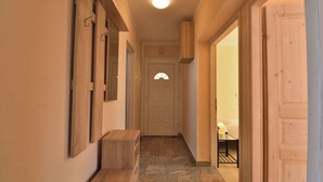 A hallway with a wooden bench, a door with a semi-circular window, and a bed with a nightstand in the adjacent room. - Apartment Nadica (Fazana)