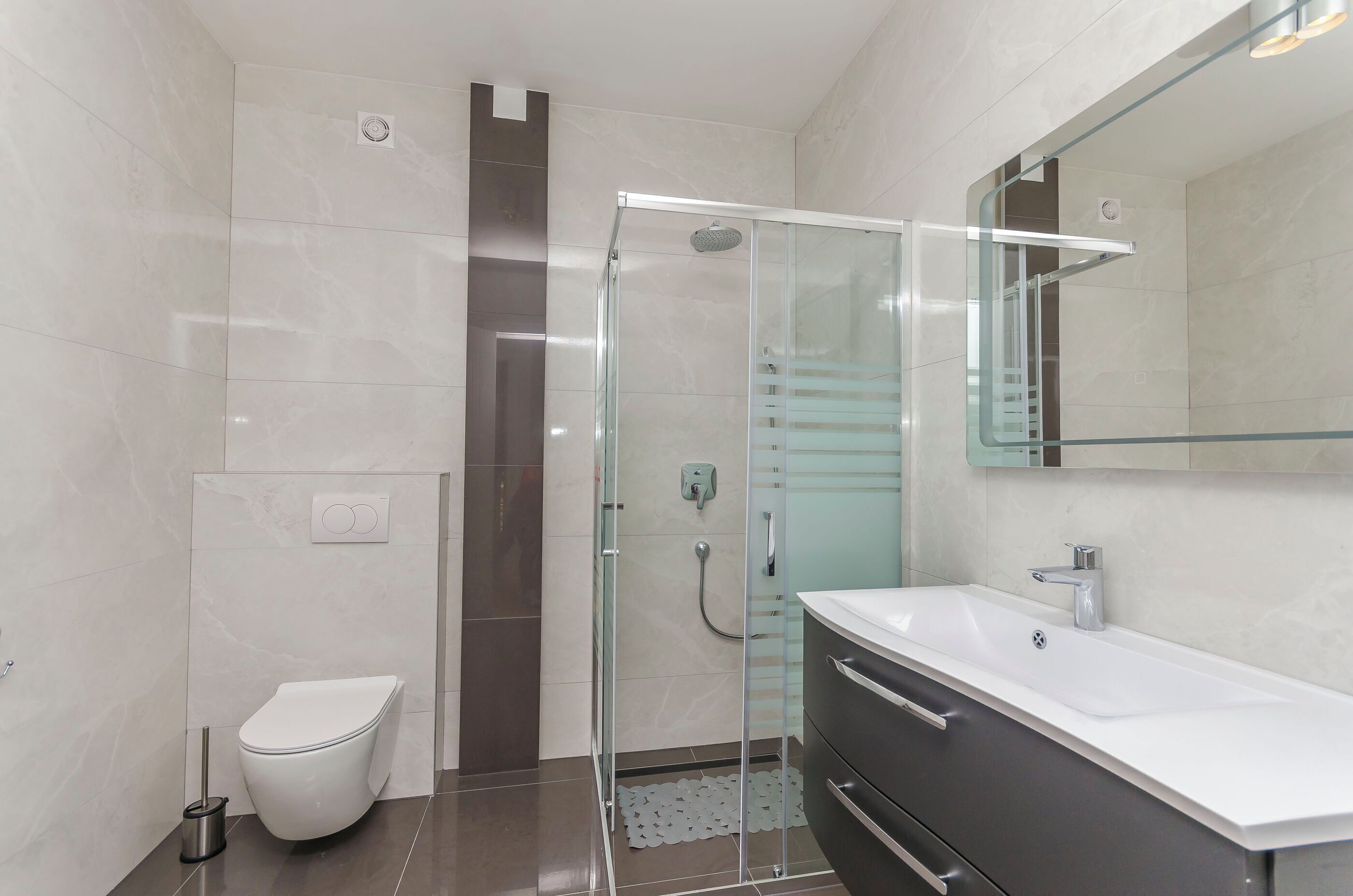 A modern bathroom with a glass-enclosed shower, a white toilet, and a vanity with a mirror.