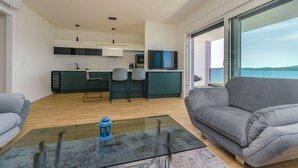 Ein modernes Wohnzimmer mit grauem Sofa, einem Glastisch und Meerblick durch große Fenster.