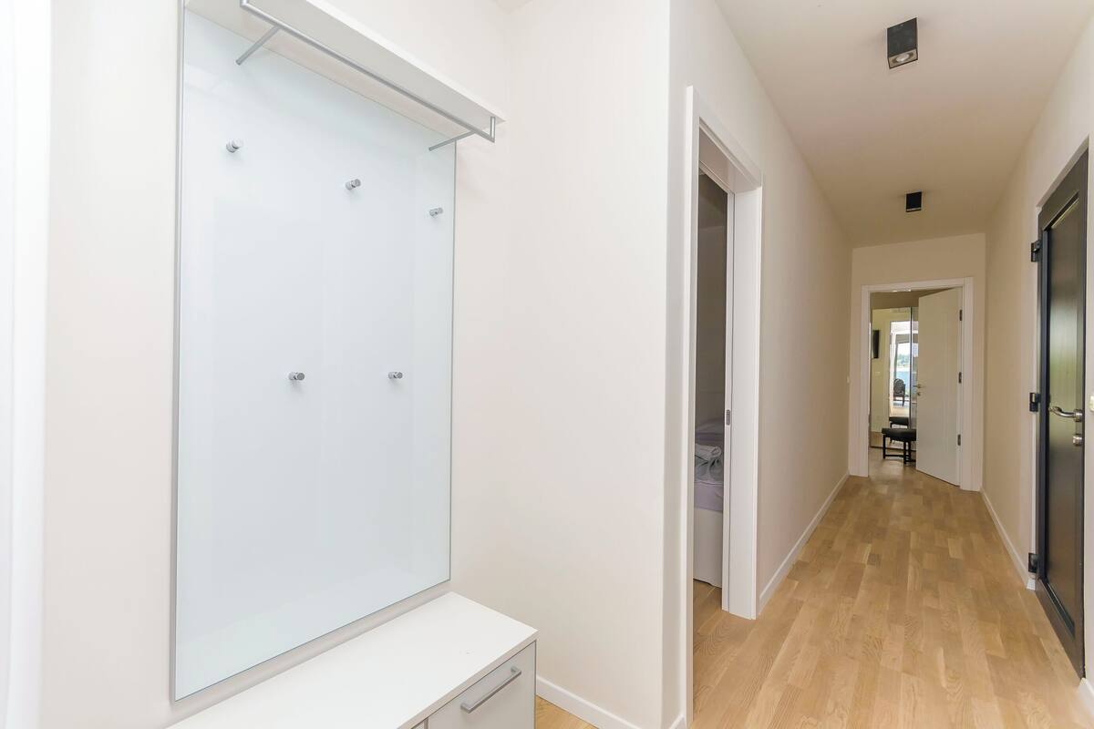 Un couloir avec une douche en verre, une commode blanche et un plancher en bois.
